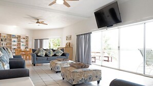 A spacious living room with a sofa set, ottomans, a flat-screen TV, and a ceiling fan. - Seaside Sanctuary 5 bed, 5 bath pool home (Tavernier)