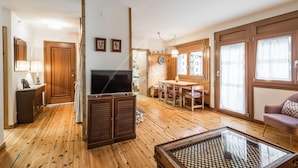 A spacious living area with wooden flooring, a television, a glass coffee table, and a dining table with chairs.