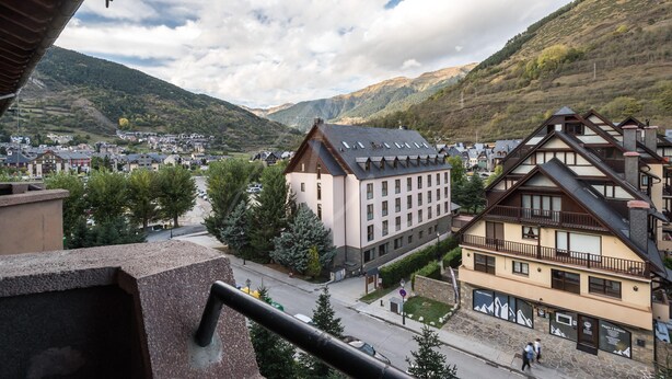 A town with traditional architecture, a prominent building with a sloped roof, and a mountainous backdrop.