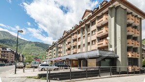 A multi-story hotel with balconies, a covered entrance, and a view of mountains in the background.