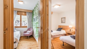 A room with two beds, a chair, and a window with curtains.