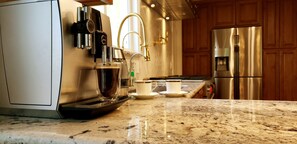A modern kitchen with a coffee machine, stainless steel appliances, and a granite countertop.