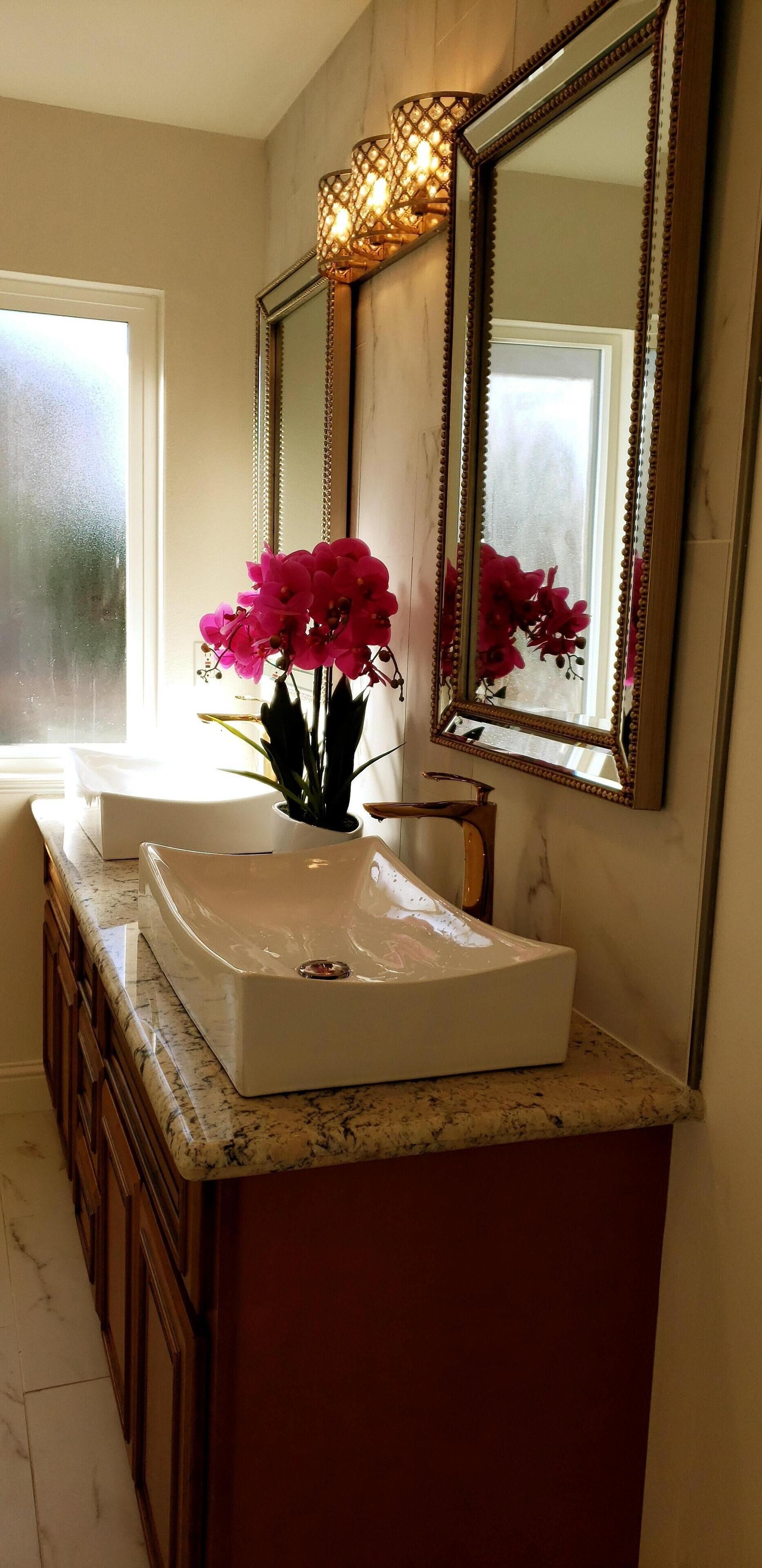 Ein Badezimmer mit zwei Waschbecken, einem großen Spiegel und einer Vase mit rosa Blumen.