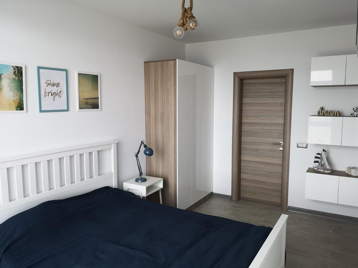 A bedroom with a bed, bedside table, lamp, wardrobe, and a door.