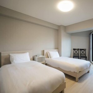A hotel room with two beds, a bedside table, a chair, and a large window.