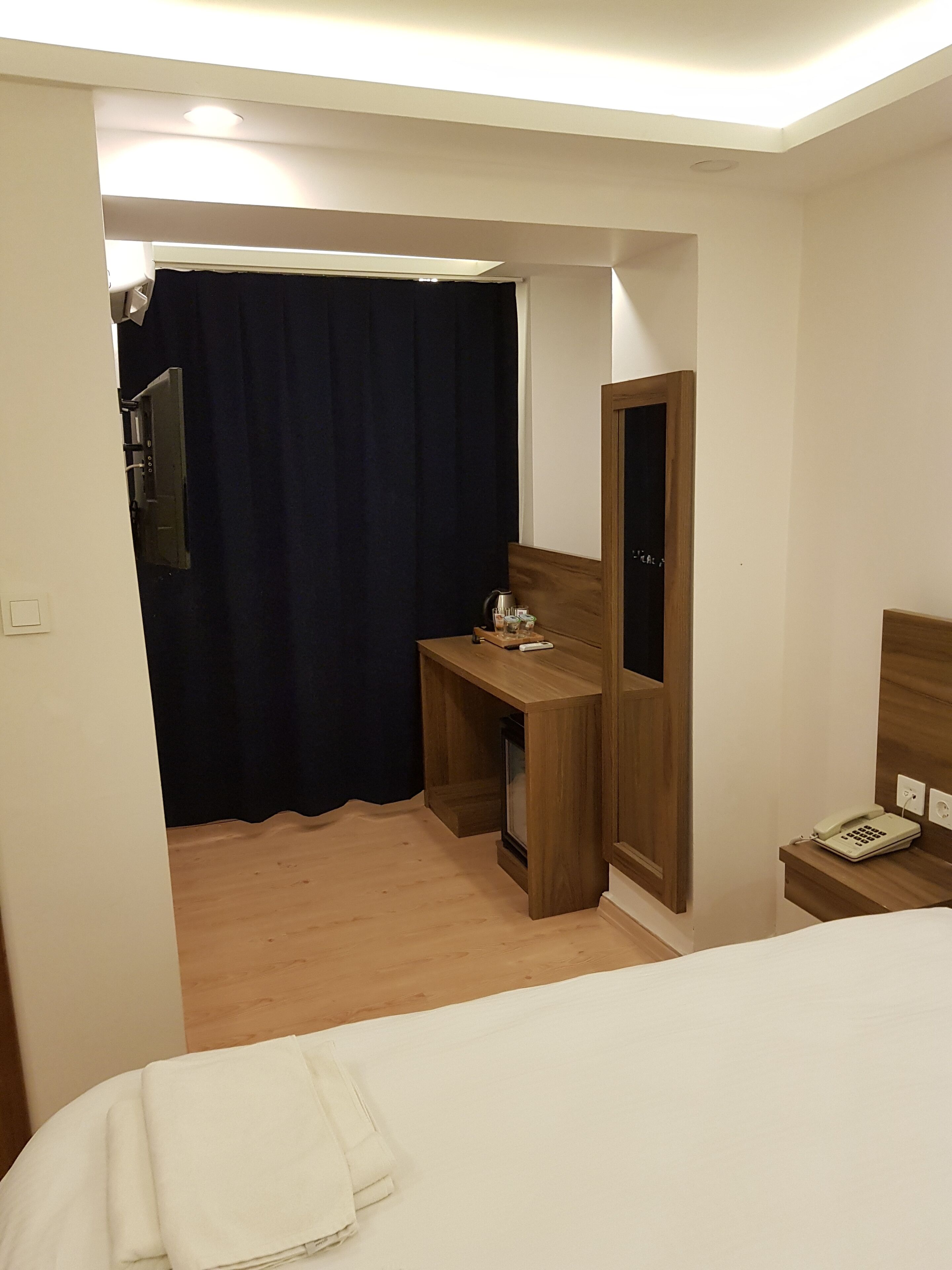 A hotel room with a bed, a desk with a chair, a mirror, a telephone, and a curtain.