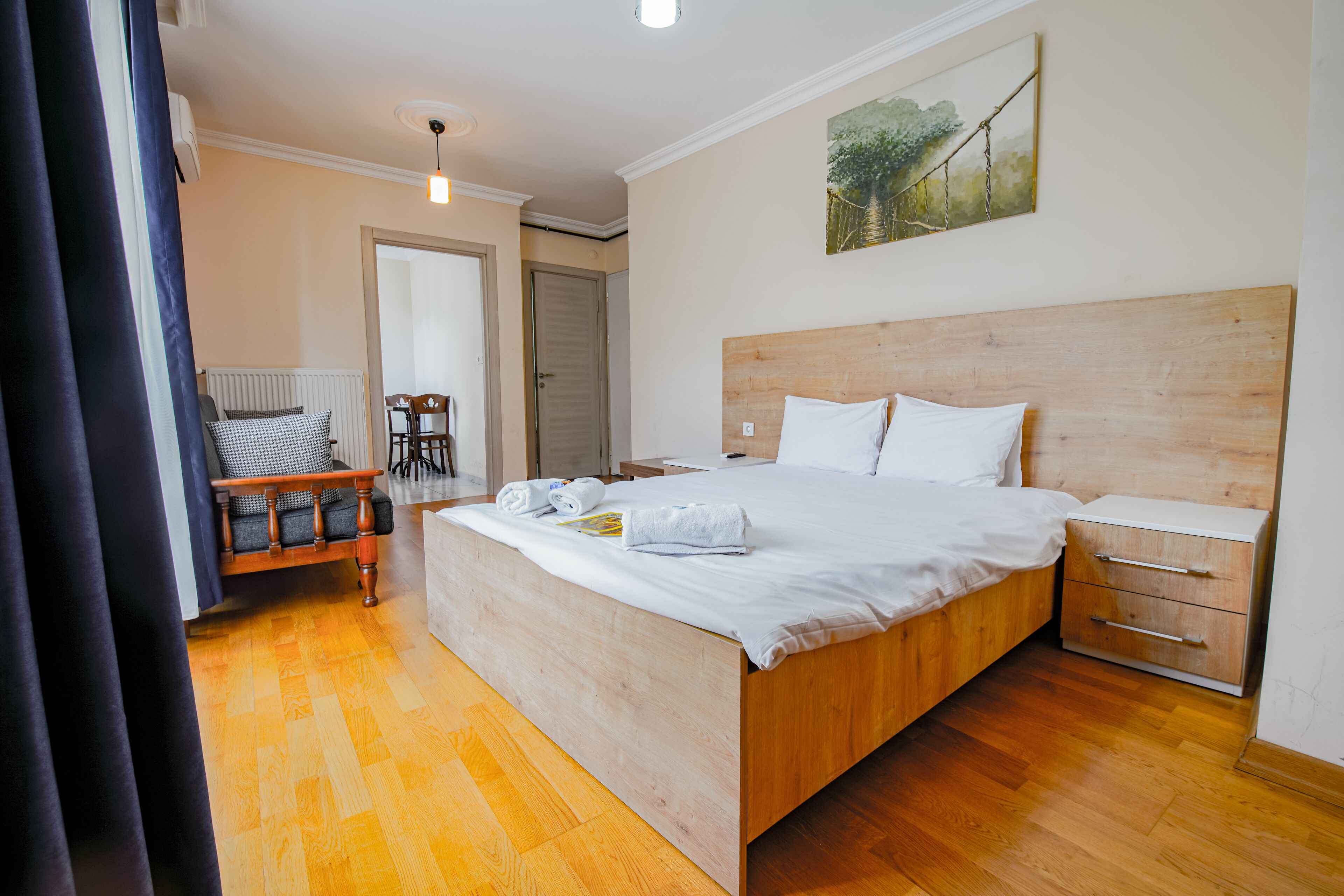 A bedroom with a wooden bed, a nightstand, a chair, and a painting on the wall.