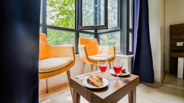 A room with two chairs, a table with a plate of food and drinks, and a view of trees through large windows. - Mitani Suites (Istanbul)