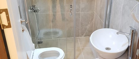 Casa de banho com cabine de duche em vidro, sanita branca e lavatório branco.