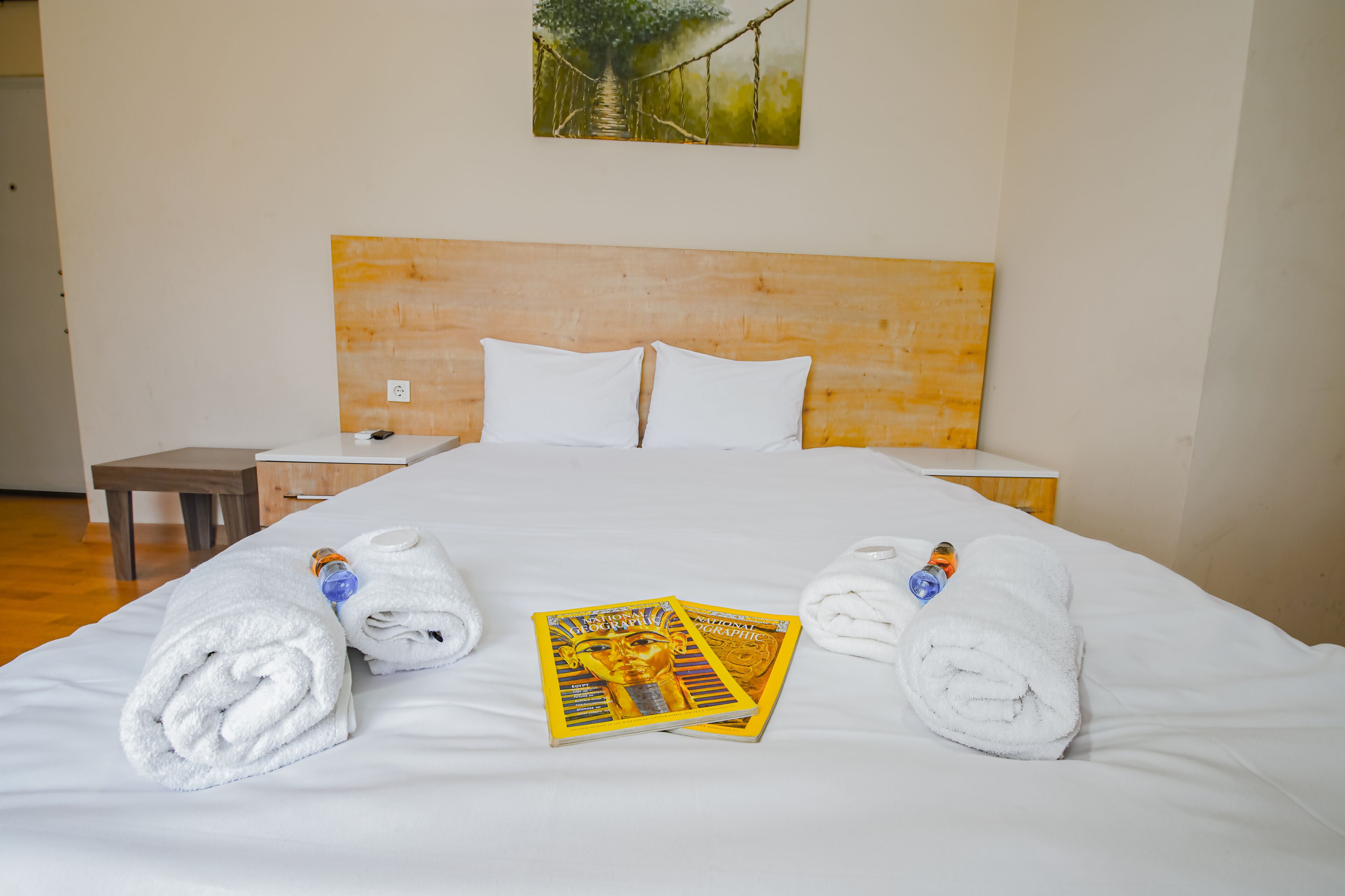 A neatly made bed with two rolled white towels and a magazine on it.