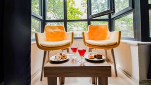 Two orange chairs with a table between them, a window with a view of trees, and a plate with pastries and drinks. - Mitani Suites (Istanbul)