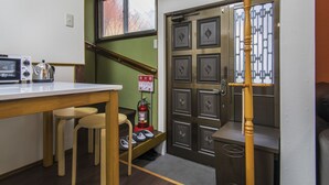 Une petite cuisine équipée d’un four à micro-ondes, d’une bouilloire et d’un extincteur. On y trouve également un porte-manteau en bois et une porte ornée d’un motif décoratif.