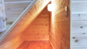 Une pièce mansardée en bois, avec des plafonds inclinés et un seul point lumineux.