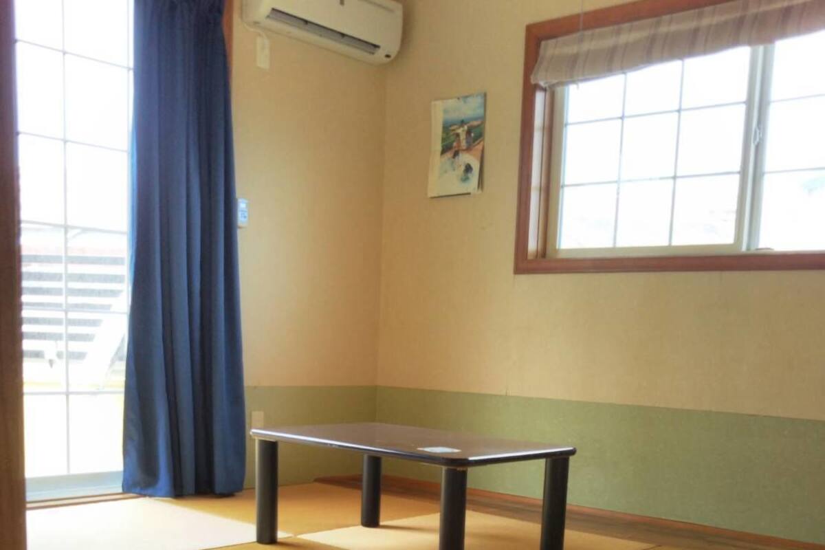 Une pièce avec un sol recouvert de tatamis, une petite table, une fenêtre donnant sur un beau paysage et un appareil de climatisation.