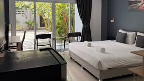 Una habitación de hotel moderna con cama, escritorio, sillas y vistas a zonas verdes a través de amplios ventanales.