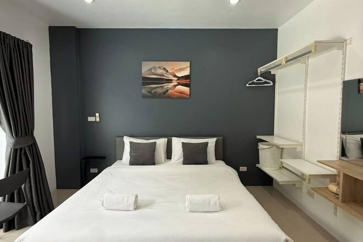 A modern hotel room with a large bed, two pillows, a painting on the wall, a chair, and a desk with a mirror.