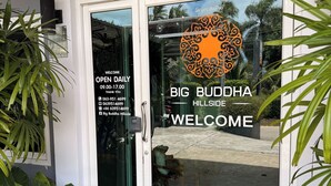 Una puerta de vidrio con un cartel de bienvenida, un número de teléfono y el horario de atención de Big Buddha Hillside.