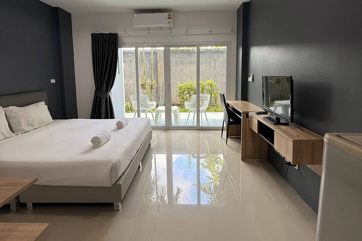 A modern hotel room with a large bed, a desk, a flat-screen TV, and a sliding glass door leading to a balcony.