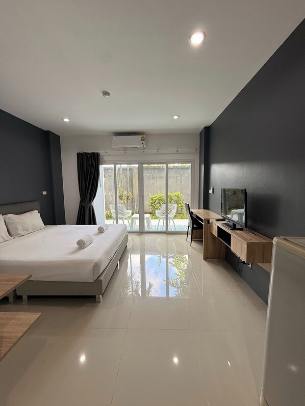A modern hotel room with a large bed, a desk, a flat-screen TV, and a sliding glass door leading to a balcony.