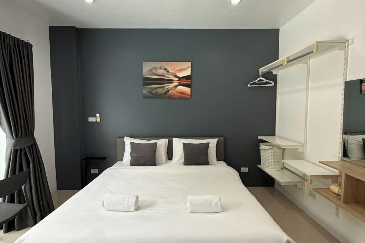 A modern hotel room with a large bed, two pillows, a painting on the wall, a chair, and a desk with a mirror.