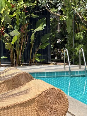 A pool area with a clear blue pool, wicker lounge chairs, and lush greenery. - Big Buddha Hillside Hotel (Chalong)