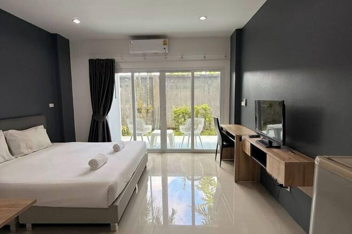 A modern hotel room with a bed, a desk, a television, and a sliding glass door leading to an outdoor area.