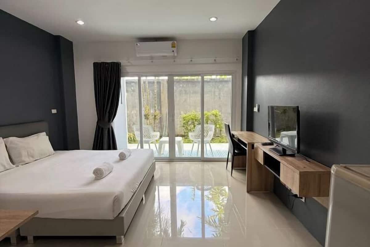 A modern hotel room with a bed, a desk, a television, and a sliding glass door leading to an outdoor area.