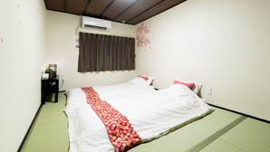 A room with a bed, a bedside table, a wall-mounted air conditioner, and a window with curtains. - Tsuruhashi Guest House (Osaka)