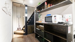 A compact kitchen with a microwave, shelves, and a staircase leading to another room. - Tsuruhashi Guest House (Osaka)
