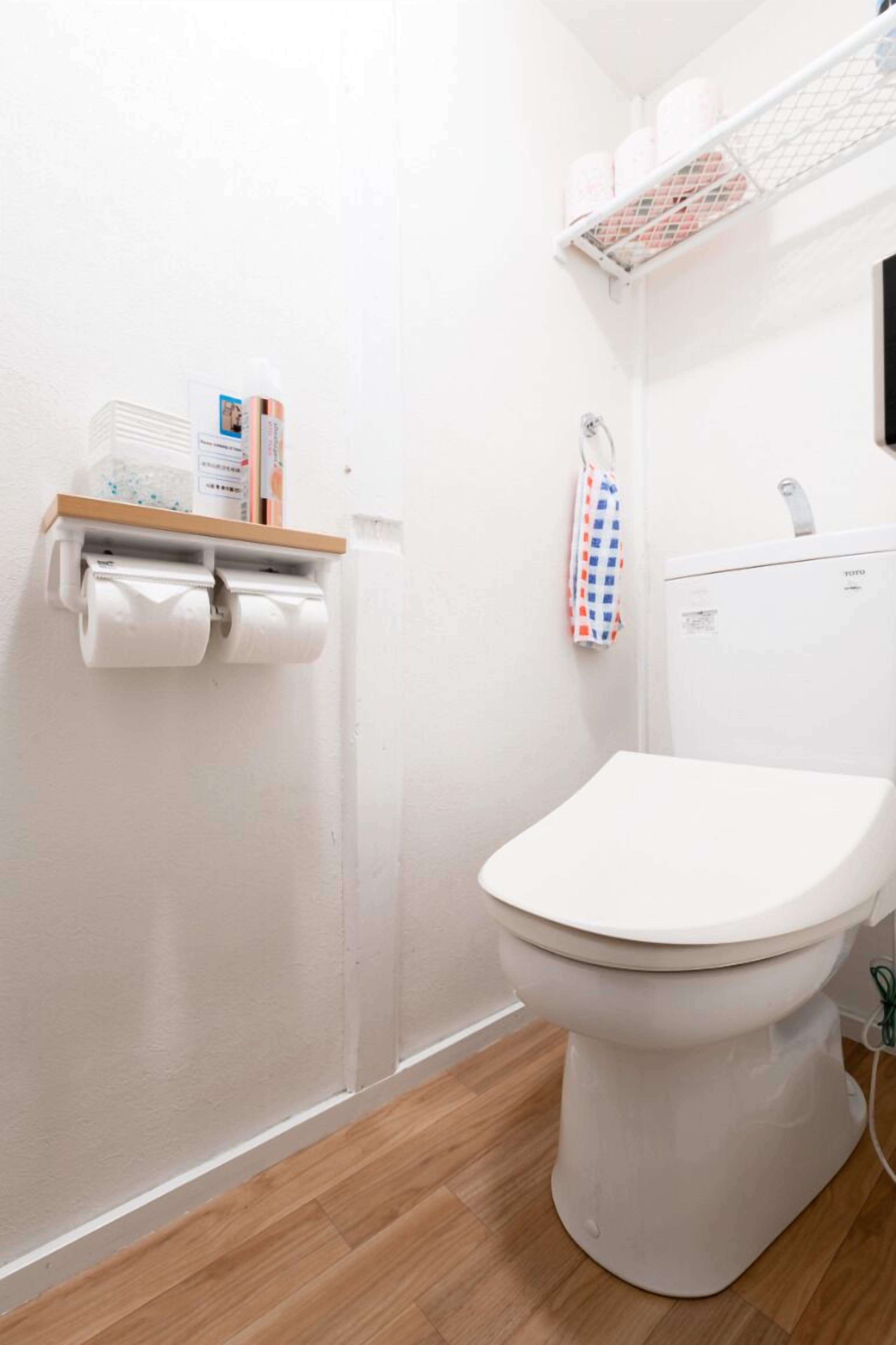 A small, clean bathroom with a toilet, a shelf with toilet paper, and a towel hanging on the wall.