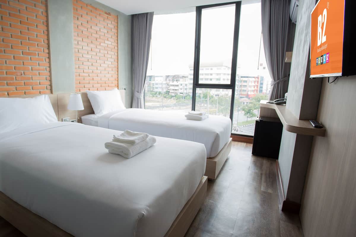 Une chambre d’hôtel avec deux lits, un mur en briques, une grande fenêtre et un téléviseur fixé au mur.