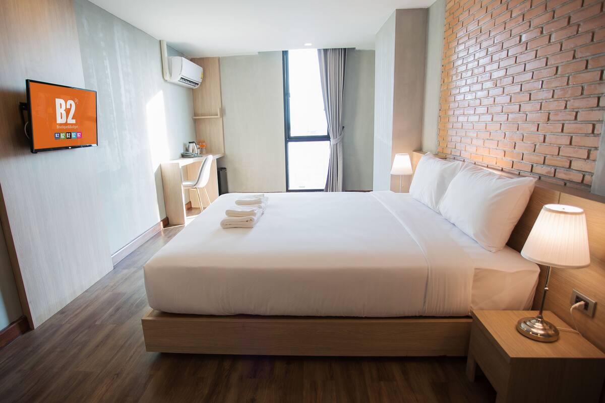 Une chambre d’hôtel avec un grand lit, un téléviseur fixé au mur, un bureau avec une chaise et une fenêtre avec des rideaux.