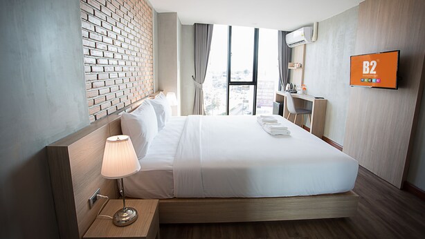 Habitación de hotel con una cama grande, una lámpara de noche, un televisor en la pared y vista a la ciudad por la ventana.