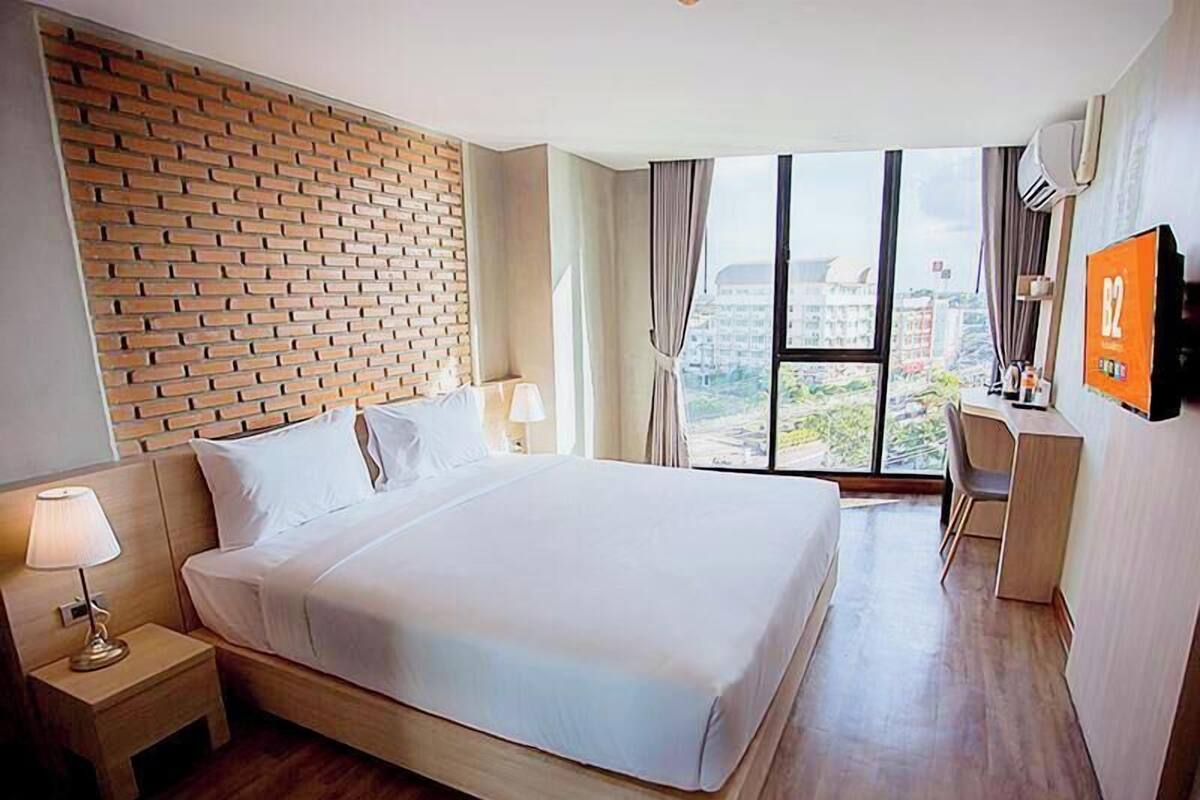 Une chambre d’hôtel avec un grand lit, un bureau, une télévision et une vue sur les immeubles grâce à de grandes fenêtres.