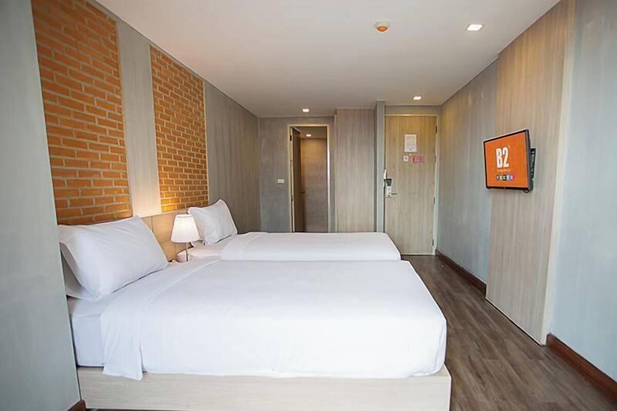 Une chambre d’hôtel avec un grand lit, une table de chevet avec une lampe, un mur décoratif en briques et une pancarte indiquant le numéro de chambre : B2.