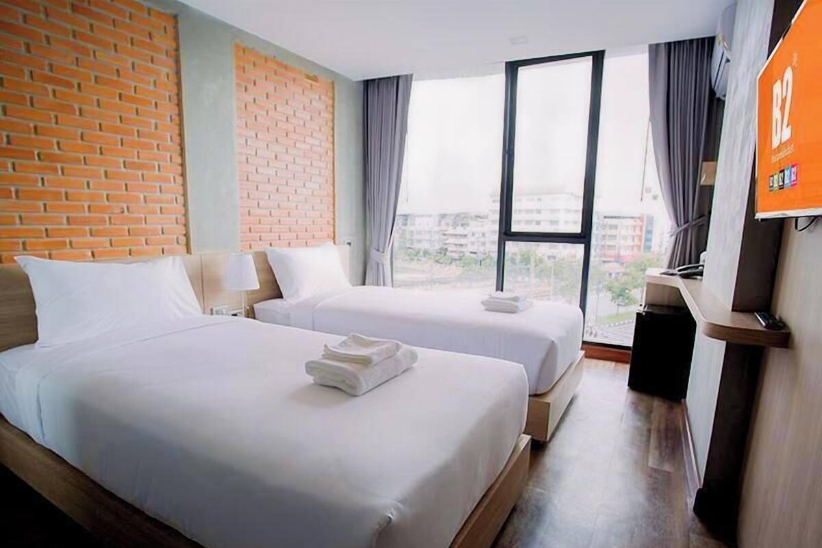 Une chambre d’hôtel avec deux lits, un mur décoratif en briques, une grande fenêtre et un téléviseur fixé au mur.