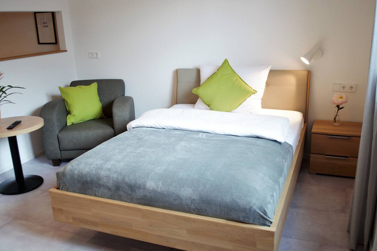 A bedroom with a bed, a chair, a small table, and a nightstand.