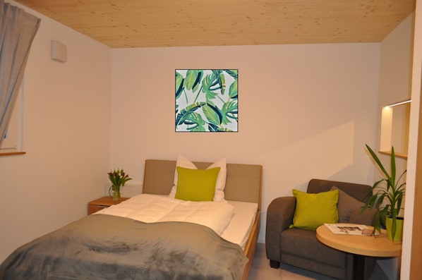 A bedroom with a bed, a sofa, a small table, and a potted plant.