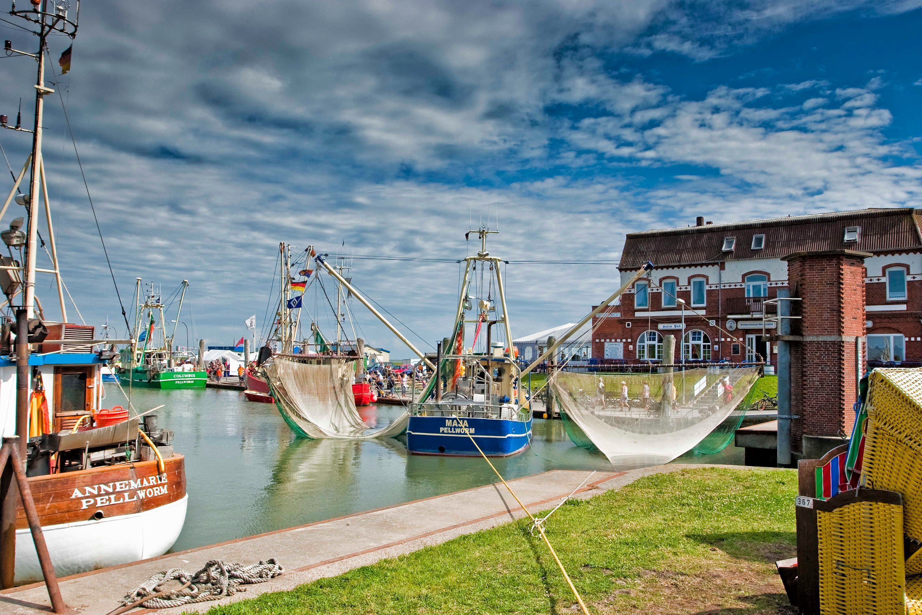 Ein Hafen mit vertäuten Booten, ein Gebäude mit roter Backsteinfassade und eine Wiese mit gelbem Zaun.