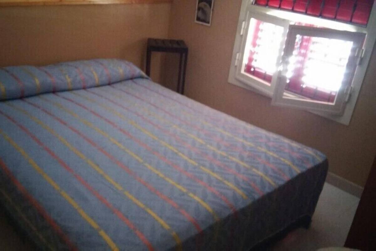 A bedroom with a bed, a window with red curtains, and a small wooden stool.