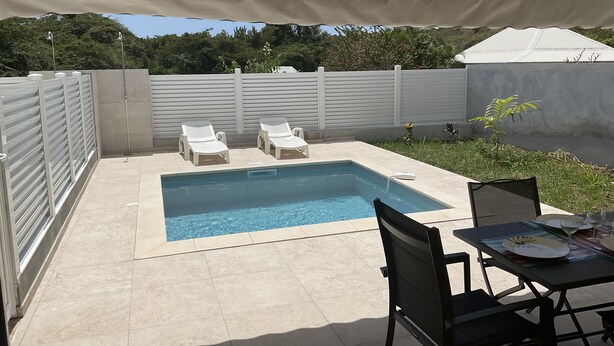 A swimming pool with two lounge chairs, a table with plates and glasses, and a covered area with a tent. - Villa Bougainvilliers with private pool in Le Diamant (le diamant)