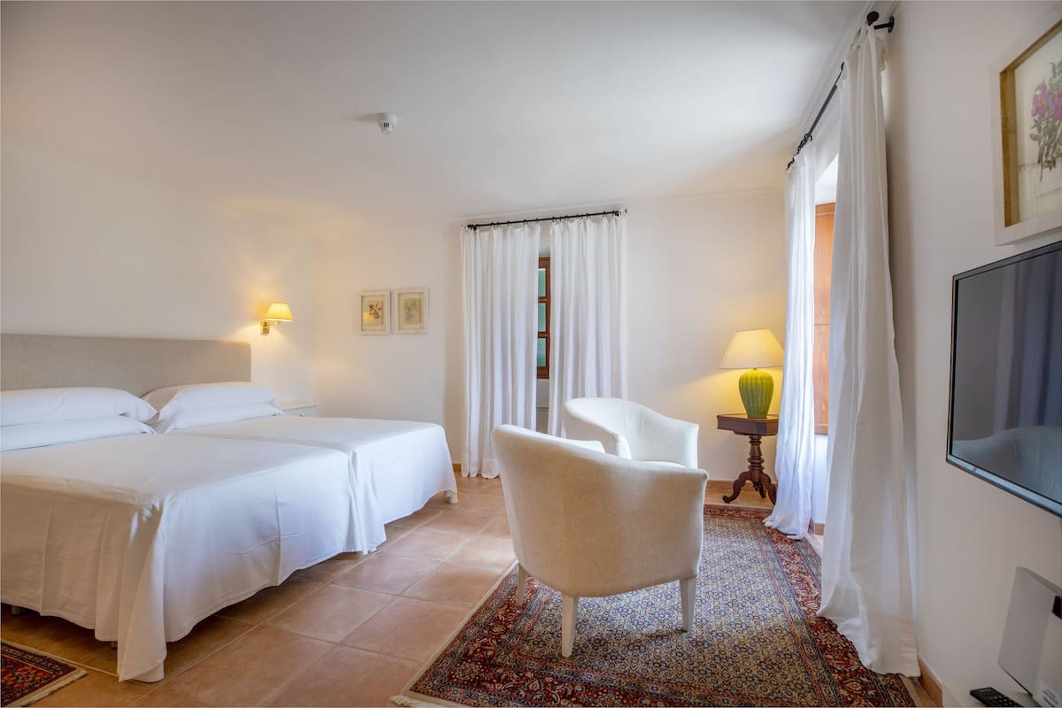 A hotel room with two beds, a chair, a TV, and a lamp.