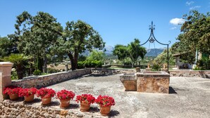 Una terraza en la azotea con flores rojas en macetas, bancos de piedra y vistas a montañas distantes.