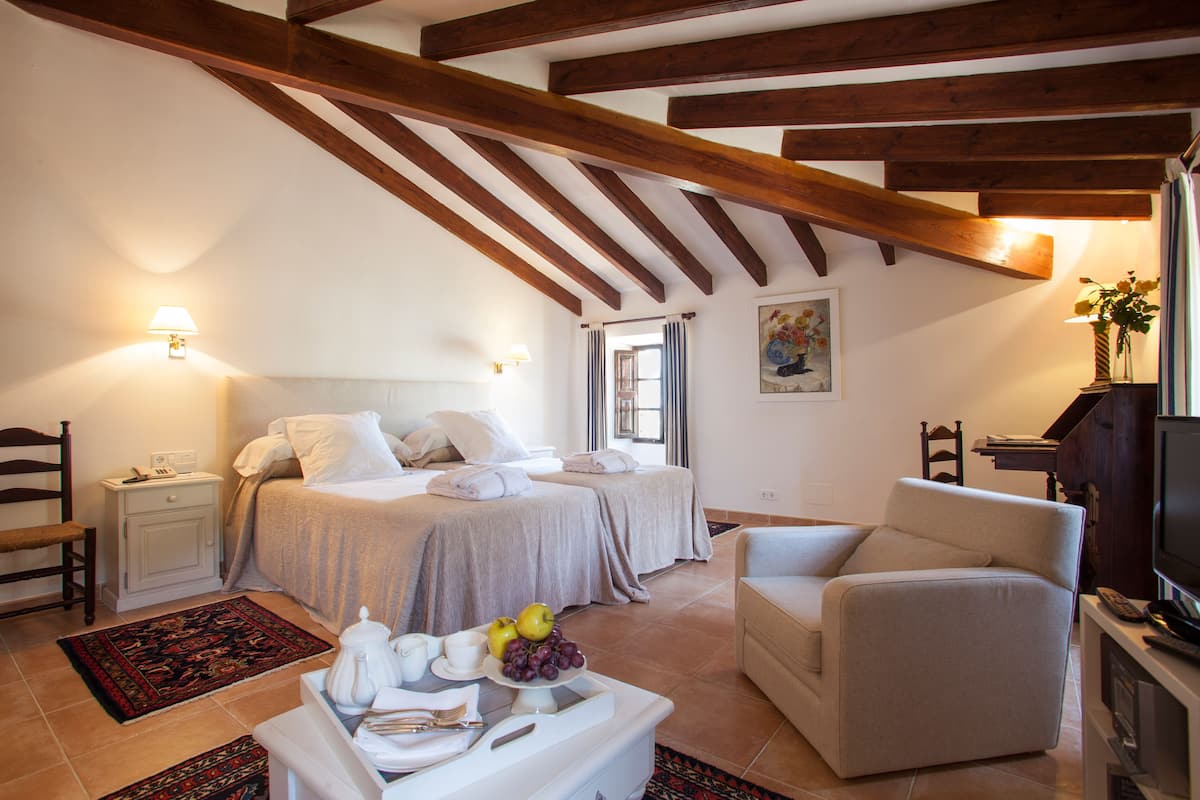 A bedroom with two beds, a sofa, a TV, and a dining area with a table set for two.