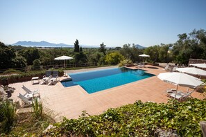 A rectangular pool with clear blue water, surrounded by a tiled patio area with lounge chairs and umbrellas. - Hotel Llenaire (Pollenca)