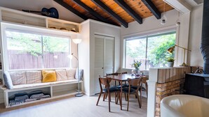 Een gezellige woonkamer met een ingebouwde bank, een eettafel met stoelen, een open haard en grote ramen met uitzicht op de omgeving.