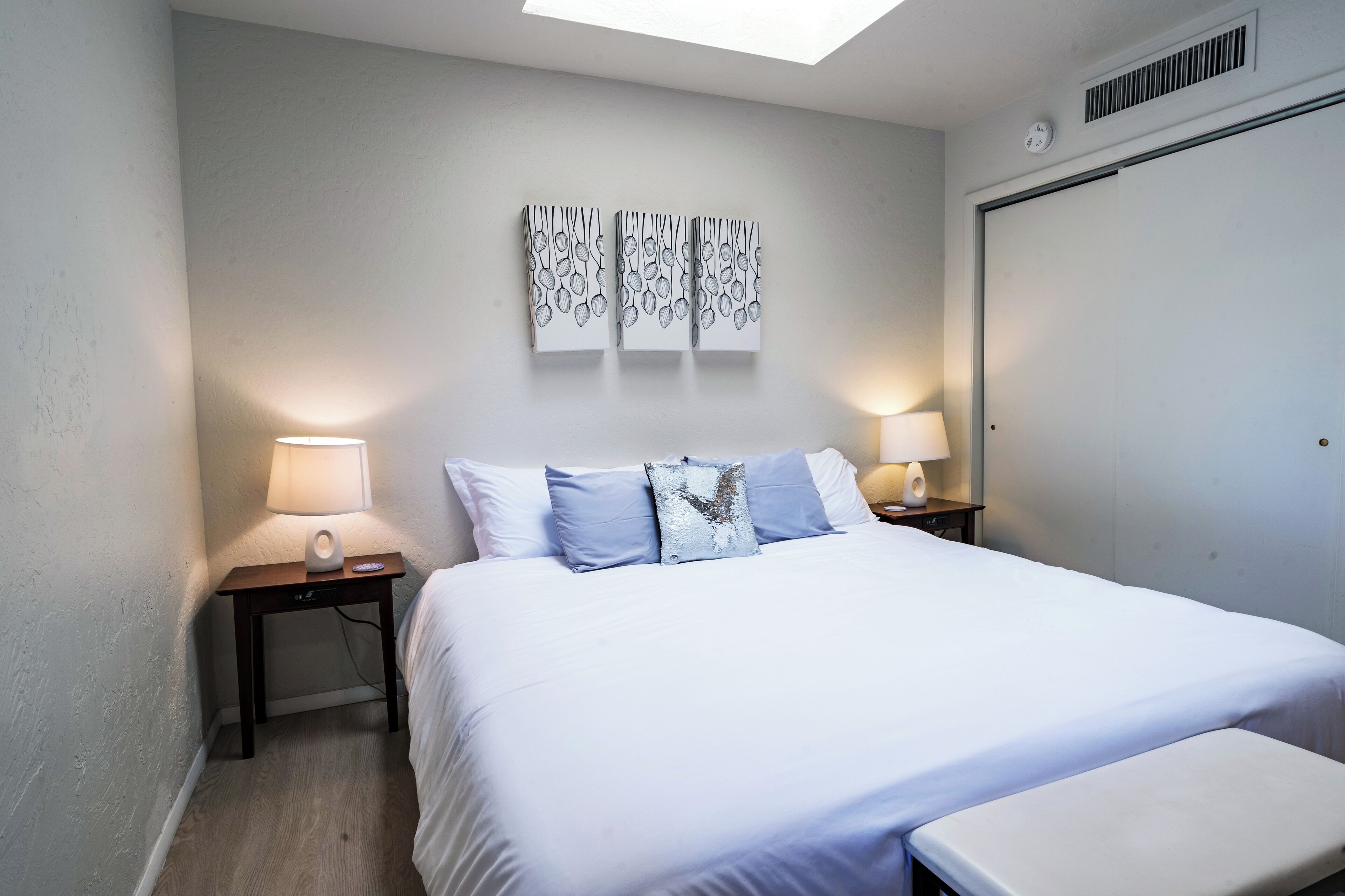 Een slaapkamer met een bed, twee nachtkastjes met lampen, een wandklok en een deur.