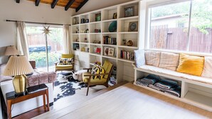 Een gezellige woonkamer met een houten plafond, een grote boekenkast, een comfortabele bank en een raam met uitzicht op een houten schutting.
