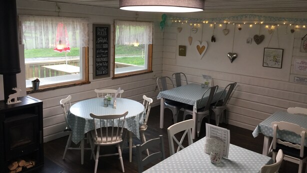 A cozy dining area with round tables and chairs, a large window with curtains, and heart-shaped decorations on the wall.