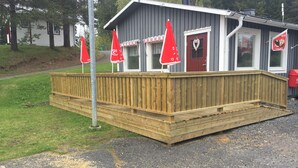 A wooden deck with a building featuring a red door and windows, and red flags on poles.